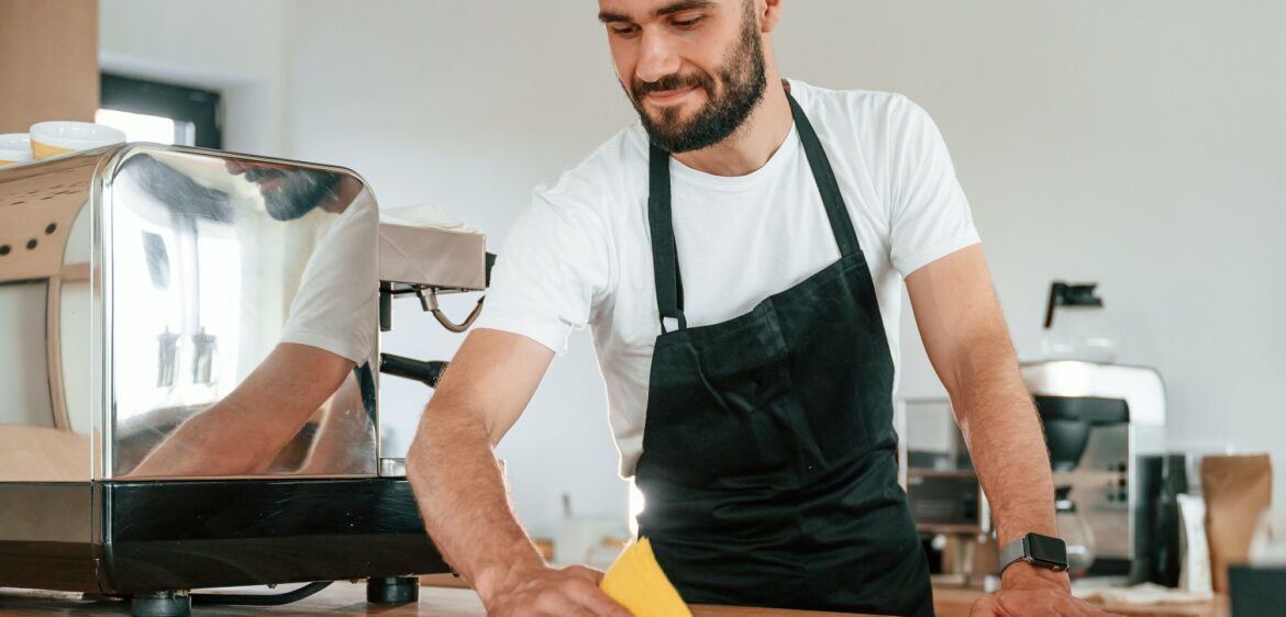 Cleaning table. Cafe worker in white shirt and black apron is indoors