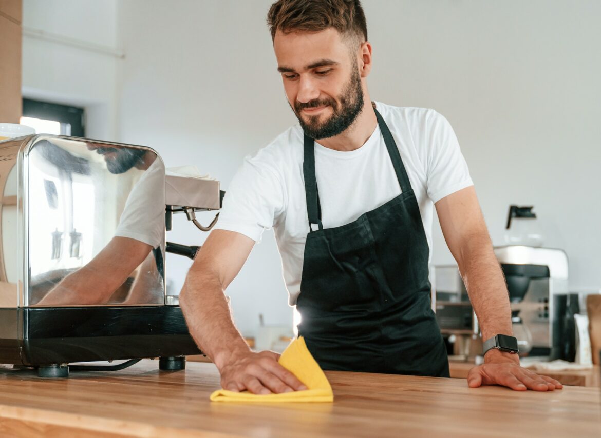 Cleaning table. Cafe worker in white shirt and black apron is indoors