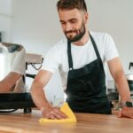 Cleaning table. Cafe worker in white shirt and black apron is indoors