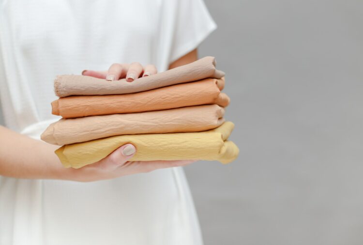 cropped image of smiling seamstress holding stack of colored fabric