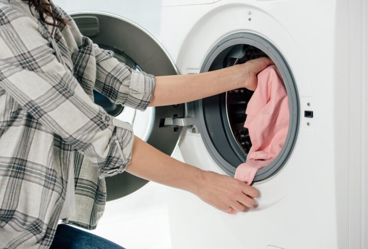 cropped view of woman putting clothes in washer in laundry room