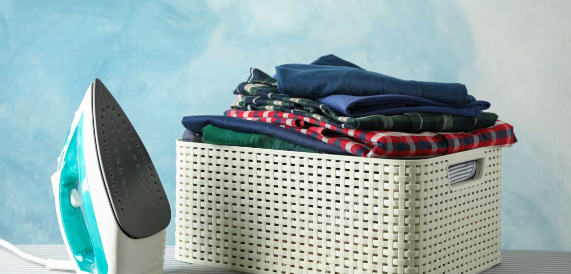 Iron and basket with clean shirts on ironing board, copy space