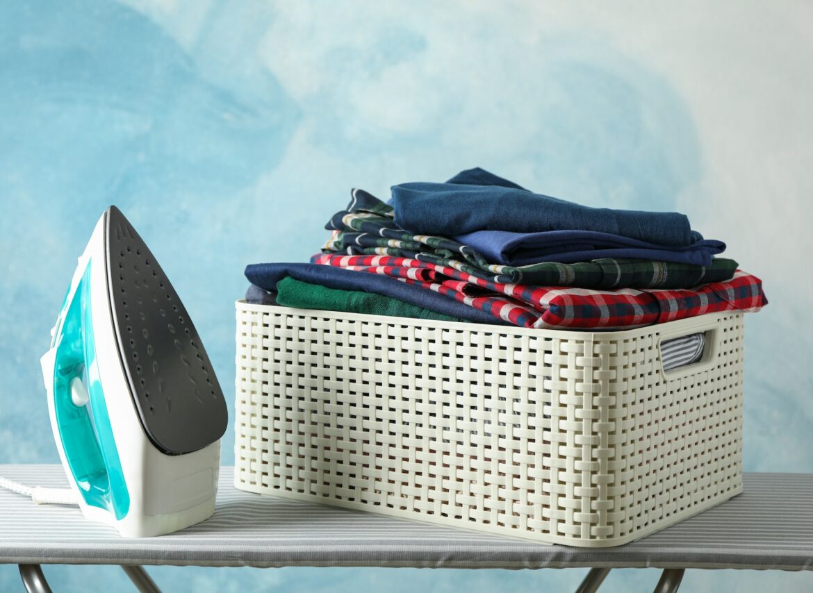 Iron and basket with clean shirts on ironing board, copy space