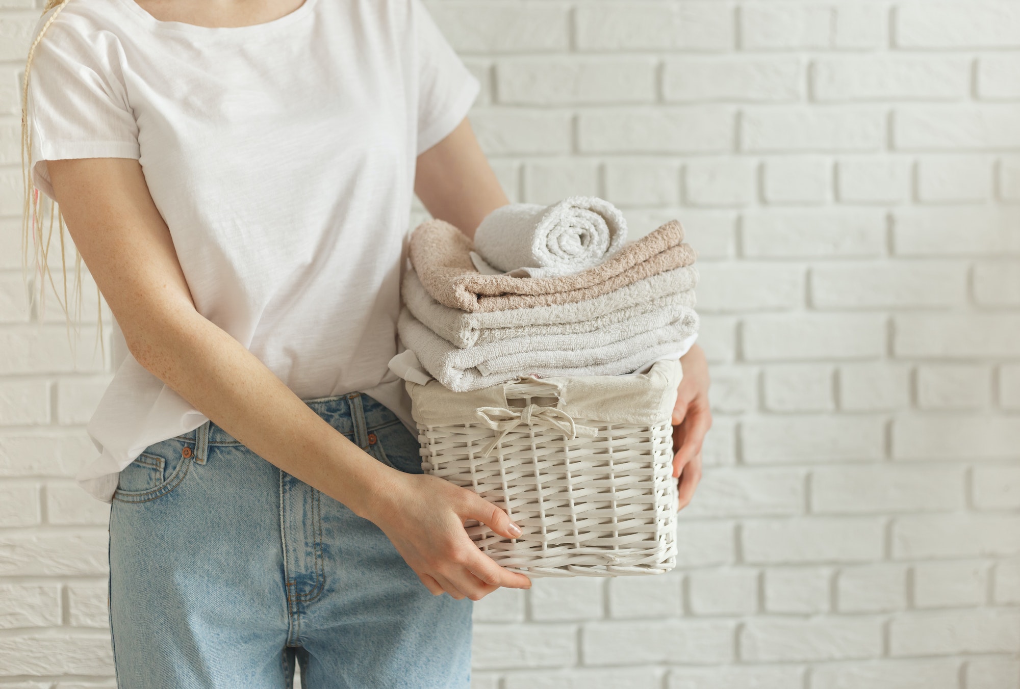 Woman holding basket with heap of different clothes, on bricks wall background