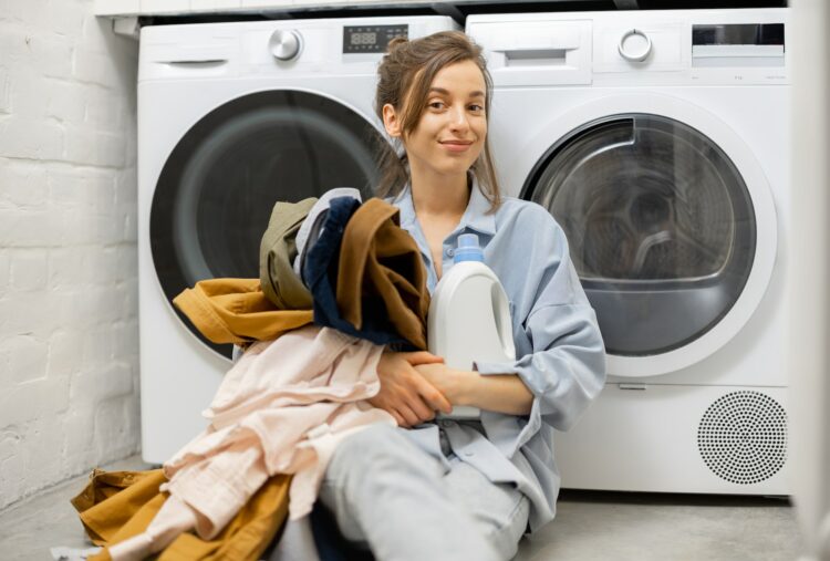 Woman with clean clothes and detergent in the laundry room at home