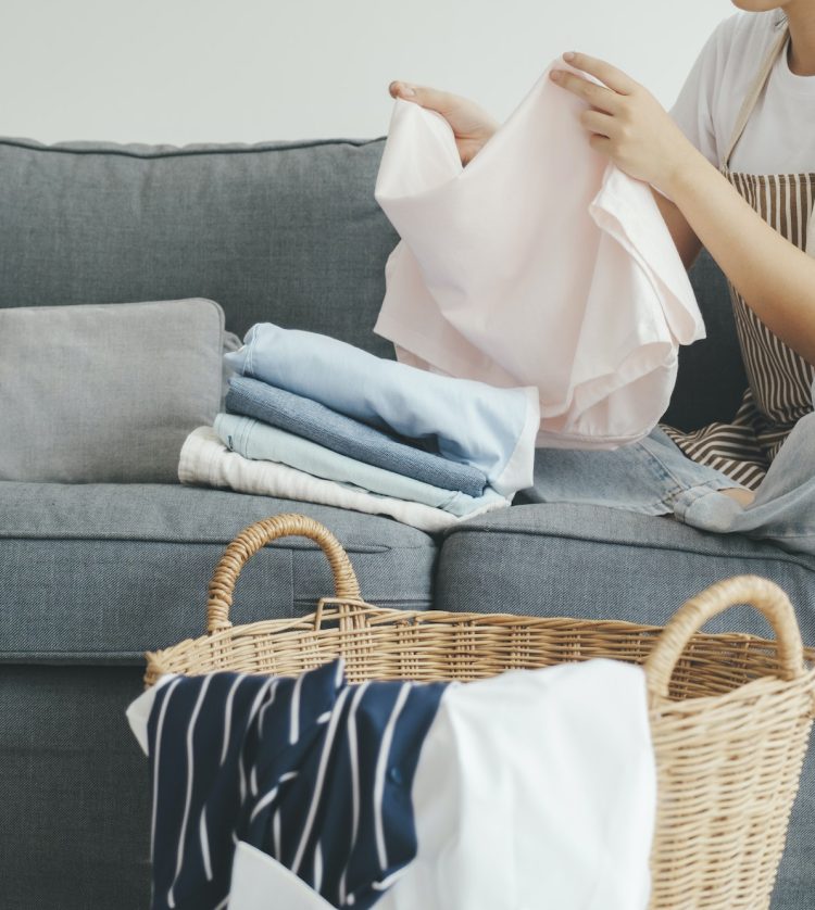 Young woman folding clothes on sofa at home.