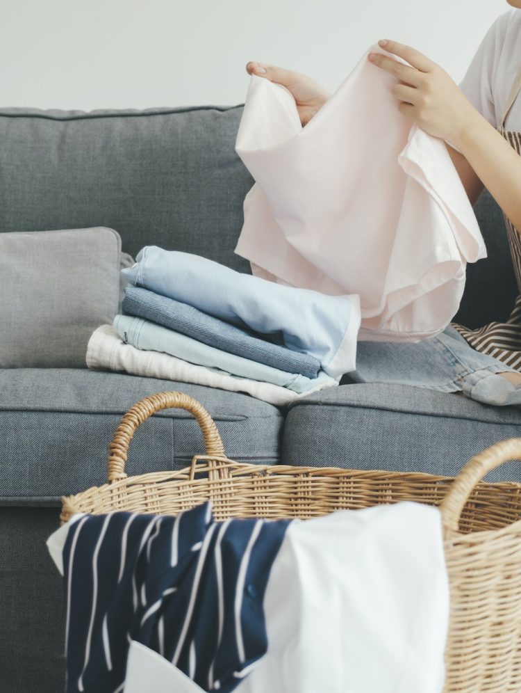 Young woman folding clothes on sofa at home.